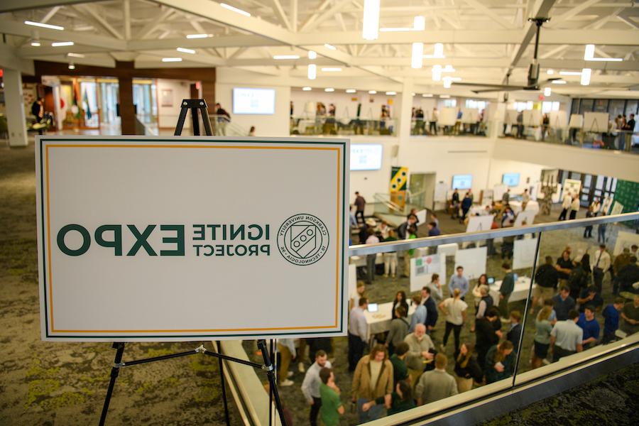 At Clarkson University a sign reading “Ignite Project Expo” is displayed on a balcony, while students, faculty, and staff can be seen interacting near poster boards on the floor below.